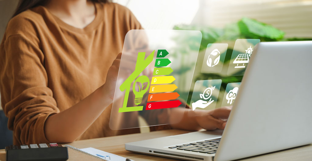 Auditeur énergétique réalisant des mesures avec une caméra thermique sur des équipements industriels dans un local technique d'entreprise, environnement professionnel authentique avec tuyauteries et armoires électriques visibles